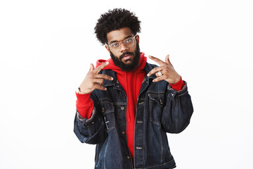 Celebrity posing paparazzi. Self-satisfied cool and arrogant african american bearded male rapper with afro hairstyle showing v signs or yo gesture as posing stylish and confident over gray wall - obrazy, fototapety, plakaty