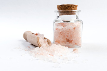 Fototapeta na wymiar Himalayan pink salt in wooden scoop and jar on isolated on white background. Closeup.