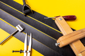 Leather craft tools and leather stripes for belt on a yellow background. Handmade and hobby theme