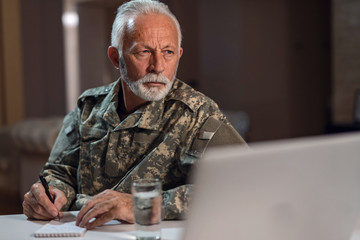 Pensive senior sergeant taking notes at office desk.