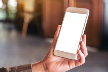 Mockup image of hand holding and showing a white mobile phone with blank screen with blurred background in cafe