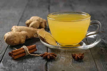A drink of ginger root and citrus and a bunch of cinnamon sticks on a black wooden table.