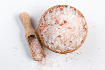 Himalayan pink salt  in wooden bowl and scoop isolated on white background. Closeup.