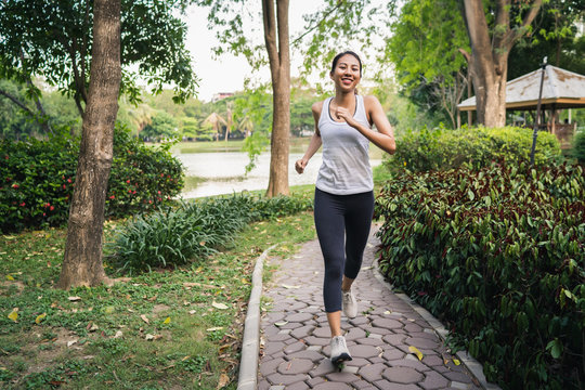 Healthy beautiful young Asian runner woman in sports clothing running and jogging on sidewalk near lake at park in the morning. Lifestyle fitness and active women exercise in urban city concept.