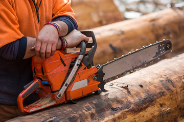 Close up view of hands resting on a chainsaw which in turn is resting on a log