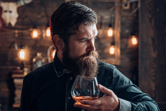 Man With Alcohol Drink At Home. Bearded Man Sitting At Bar. Alcoholic With Bottle And Glass Drinking Cognac At Night.