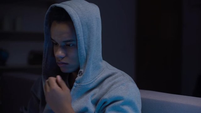 African-american teen boy sitting in dark room suffering depression, loneliness