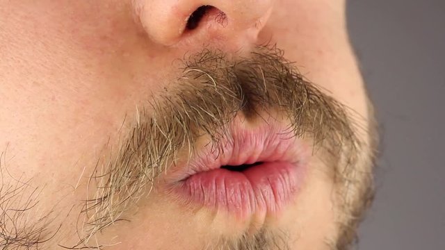man with a mustache and beard strongly blows on the camera, puffs his cheeks, like a blows the candle out, side view, closeup