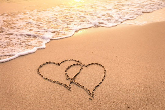 Romantic honeymoon holiday or Valentine's day on the beach concept with two hearts drawn on the sand, tropical getaway for couples, love symbol