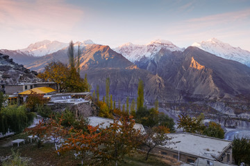 Sunrise at Hunza Nagar valley. Morning sunlight shining at snow capped Rakaposhi and Diran peaks in Karakoram mountain range,with a view of colorful trees in autumn season. Gilgit Baltistan, Pakistan.