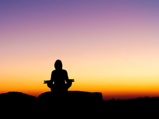 Silhouette of human doing yoga on top mountain at sunset or sunrise time