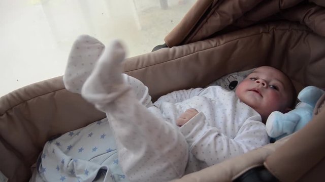 cute 3 months old baby boy making funny faces in baby carry cot