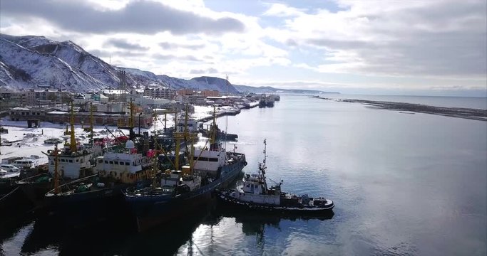 Flying above the waters of Tatar Strait, sea of Japan. Cityscape of Nevelsk (Sakhalin island, Russia), mountains landscape and fishing boats in dock are on the right. Winter. Aerial