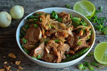 Rice noodles with fried pork in a white bowl on a wooden background