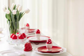 Happy easter. Decor and table setting of the Easter table is a vase with white tulips and dishes of red and white color. Easter colored eggs with white polka dots.