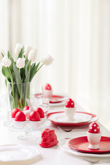 Happy easter. Decor and table setting of the Easter table is a vase with white tulips and dishes of red and white color. Easter colored eggs with white polka dots.