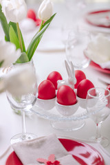 Happy easter. Decor and table setting of the Easter table is a vase with white tulips and dishes of red and white color. Easter colored eggs with white polka dots.