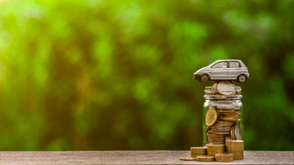 Grey miniature car model on coins glass piggy bank. - Finance and car loan, saving money for a car...