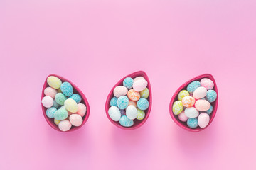 Happy Easter greeting card with small eggs in three egg shaped bowls, on pink background with copy space in flat lay