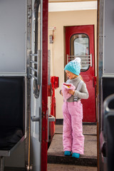 Little girl in blue cap and winter pants tarvelling by old train Kukushka in Georgia between Bakuriani and Borjomi