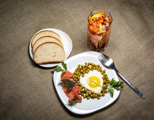 Fried eggs with peas and red fish on a white plate. Berry juice and white bread on the table. Top view.