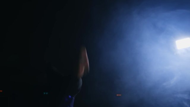 Girl gymnast performs flips on the gymnastics carpet in slow motion in the back light in the smoke