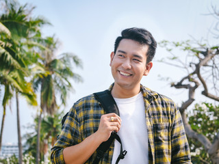 Asian man with backpack pointing to the sea with coconut tree background.