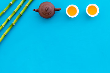 Asian tea traditions. Drink tea. Tea ceremony. Tea pot near cups of green tea and bamboo decoration on blue background top view space for text