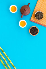 Chinese tea ceremony concept. Tea pot, tea cup, dry tea leaves, bamboo mat on blue background top view space for text pattern