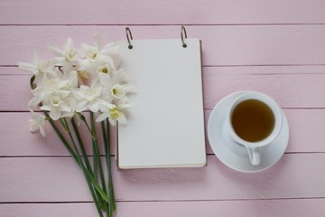 Spring tea.Flat lay.Spring to-do list.cup of tea, notebook, white daffodils bouquet on pink board wooden background..top view, copy space.Spring mood