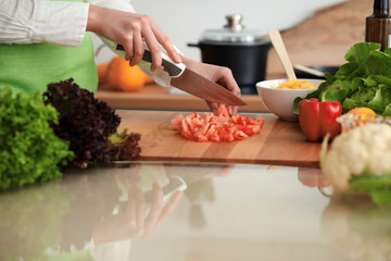 Unknown human hands cooking in kitchen. Woman slicing red tomatoes. Healthy meal, and vegetarian food concept