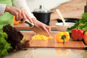 Unknown human hands cooking in kitchen. Woman slicing yellow bell pepper. Healthy meal, and vegetarian food concept