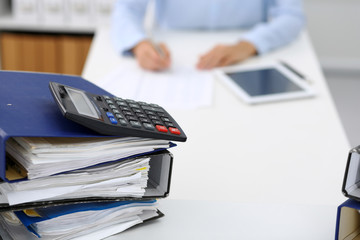 Calculator and binders with papers are waiting to be processed by business woman or bookkeeper back...