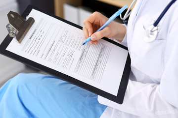 Woman doctor at work at hospital. Young female physician write prescription or filling up medical form while sitting in hospital office, close-up