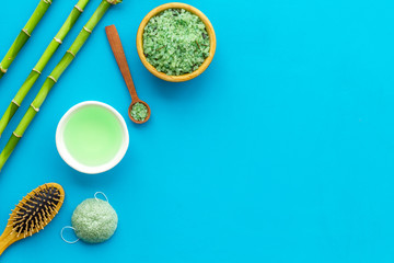 Asian spa treatment concept with natural ingredients. Spa salt, lotion, sponge near bamboo on blue background top view copy space