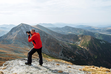 A young man sports athlete stands on the mountain and photographs beautiful landscapes
