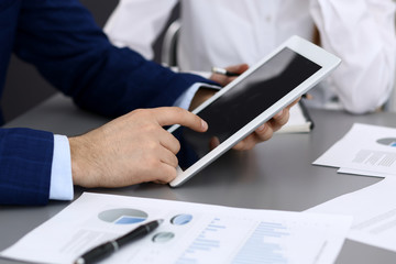 Fototapeta premium Businessman using tablet at meeting, closeup of hands. Business operations concept