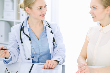 Fototapeta premium Doctor and patient talking in hospital office while sitting at the desk. Health care and client service in medicine