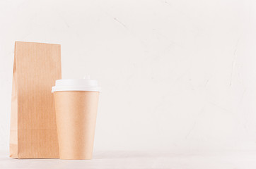 Coffee shop template for branding identity - big brown paper cup with white cap and blank kraft bag on white wood board, copy space.