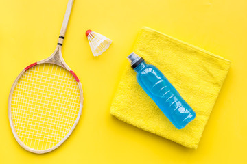 Badminton training concept. Badminton racket, shuttlecock, sport drink and towel on yellow...