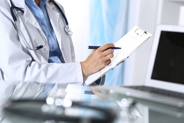 Female doctor filling up medical form on clipboard, closeup. Reflecting glass table is a physician working place. Healthcare, insurance and medicine concept