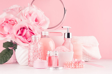 Cosmetic products for aromatherapy, spa salon - essential rose oil, bath salt, cream, soap, bath accessories with round mirror, roses in pink color on white wood board.