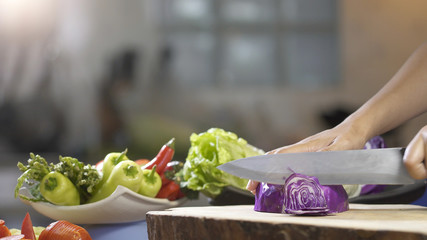 Slicing purple cabbage with kitchen knife on wooden board, close up
