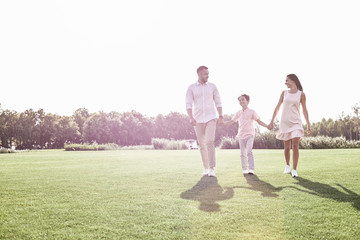Family walk. Family of three walking on grassy field smiling che