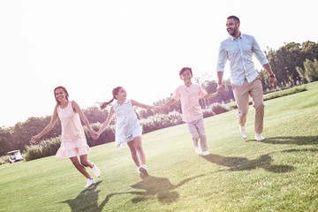 Naklejka na ściany i meble Bonding. Family of four running on grassy field smiling cheerful