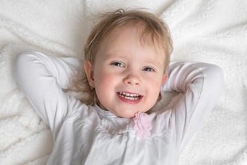 Smiling child is lying on back on white blanket