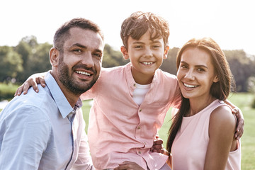 Bonding. Family of three walking on grassy field son hugging par