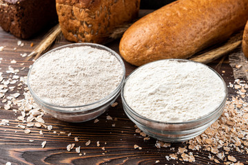 Rye and wheat flour with bread on dark wooden background.