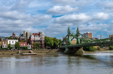 Fototapeta premium The Hammersmith Bridge, a suspension bridge that crosses the River Thames in west London. Hammersmith is in the background, photo taken from Barnes.