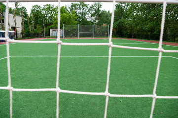 View through the net at artificial turfed playing field and white football goal